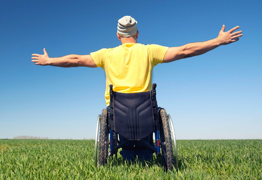 homme tourné de dos en fauteuil roulant avec les bras ouverts en signe de liberté