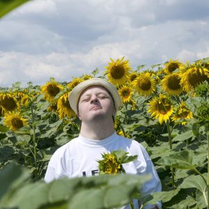 Young man with down syndrome resting and happy as the sun in the blooming field homme avec le syndrome de down dans un champ de tournesol
